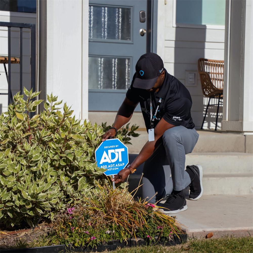 An Elite Home Pro placing an ADT yard sign in front of a home